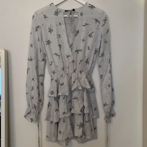 Motel blå volang klänning med blommor  - Motel blå volang klänning med blommor   Öppen fram med knytning vid halsen   Aldrig använd 