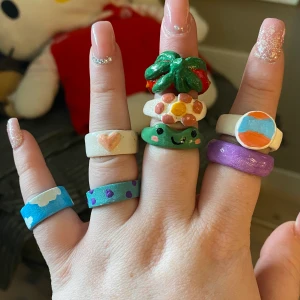 ringar - Jag gjorde dessa ringar med lera för ca ett år sedan och använder aldrig dem. så tänker sälja dem. 3kr st ( grodan & jordgubben kostar 10kr st )  ( men alla för 35kr ) 🎀 hör av er vid intresse 💋alla är ganska små, förutom jordgubben + grodan 
