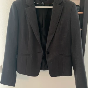 Grå damkavaj - Oanvänd kavaj från H&M. Lätt vadderad i axlarna. Figursydd. Kortare modell som slutar vid höfterna. Köparen betalar frakt