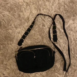 Handväska - Säljer denna svarta handväska från Gina tricot. Bra skick med lite slitningar vid handtaget med knappar, det långa bandet har inga effekter, köpt för ungefär 300kr❤️ Hör av er vid frågor!