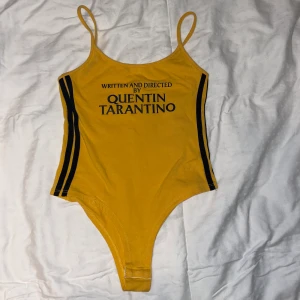 Gul body - Kill Bill body med texten ”WRITTEN AND DIRECTED BY QUENTIN TARANTINO”. Står ingen storlek men gissar på S. String formad.