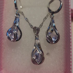 Halsband med hänge och öronhängen med zirkonia stenar - Hej! Jag vill sälja ett helt nytt halsband med hänge och öronhängen med vackra gnistrande zirkonia. Färgen skiftar från vit till blå, beroende på ljuset. Kedjans längd: 45cm. Båda hänge och öronhängen utan ögla: 2cm. Allt stemplat silver 925. Julklapp.