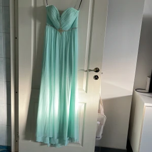 Aftonklänning  - Mintgrön aftonklänning. Axelremslös, hjärtformad urringning. Strass både vid bröstet och baktill. Städning med dragkedja baktill 