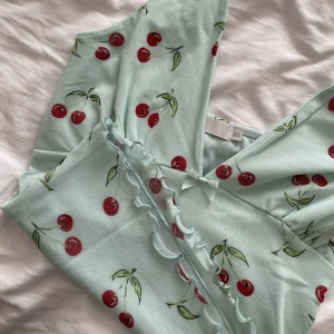 Körsbärs linne  - Ett linne med öppen rygg med söta körsbär. Mint grön med dubbeltyg och finns inga defekter. Säljer eftersom den sitter för tajt på mig. Vet tyvärr inte märket. Köparen står för frakten💗