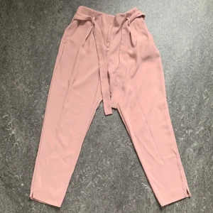 Rosa byxor storlek 34 - Fina rosa byxor from River Island i storlek 34. Liten slits längst nere och gummiband i midjan på baksidan. En väldigt liten fläck på framsidan uppe vid dragkedjan (se tredje bilden), annars i bra skick! Frakt tillkommer. 