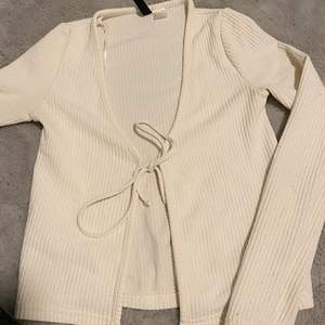 En vit blus/kofta som du kan knyta i mitten, fint att ha en tröja under. Tunnt och fräscht tyg. ( det finns ett litet hål på sidan av blusen/koftan) 