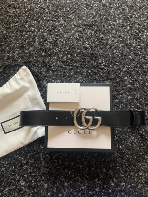 Gucci bälte  - Helt oanvänt Gucci bälte i svart med silver. Kvitto finns samt sitter blomberingen kvar. Ny pris 4000kr. Box och dustbag ingår.