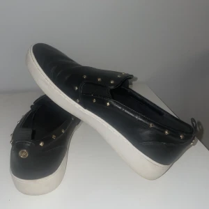 Michael kors skor - Slip in skor från Michael Kors, använtskick. Små repor på ena skon - syns endast lite utan blixt . Svarta med nitar 