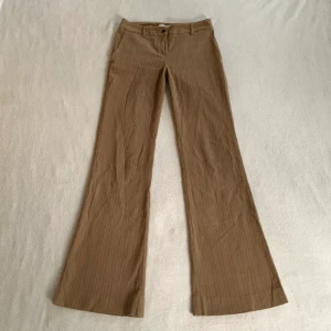 Lågmidjade byxor - Lågmidjade utsvängda randiga brun/beiga byxor, från märket Kookai! Jag är 173 cm, midjemåttet är 72 cm och innerbenslängden är 80 cm 💞(en knapp på fickorna skiljer sig lite)