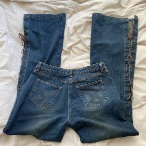 vintage jeans i y2k stil med läder snörning på benen. köpt secondhand men använd ett fåtal gånger. low waist och flared, midjemått 76cm och innerbenslängd 80cm. inga defekter, jätte bra skick!