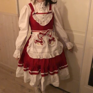 Lolitaklänning - Lolita-set/Rödluvan-dräkt från Lolitain.Man får med en blus,ett förkläde,en Jsk,en luva och rosetter(finns 26 stycken).Jag har lagt till saker tex pärlor på förklädet, förlängt klänningen och bytt knappar.Finns defekter,kontakta mig för mer info.