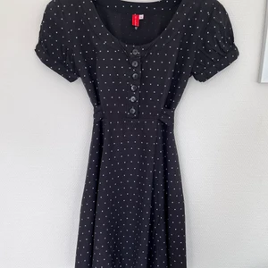 Kort prickig klänning - Kort figursydd svart klänning m vita prickar. Fint klockad med skärp. Figurnära på överkropp. Lite puffärm. Lite i modellen av 60-talet. 