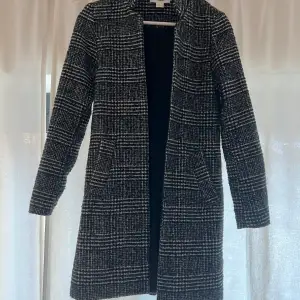 En fin grå, vit, svart mönstrad kappa från H&M, endast använd några gånger.  Storlek 32, men passar även en som har storlek 34.  Obs; denna kappa har ingen knapp. Passar som vårkappa eller höstkappa. 