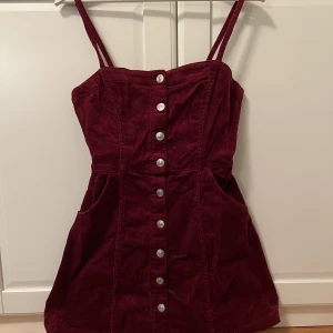 Manchesterklänning från H&M - En vinröd manchesterklänning frpn H&M. Den är i minilängd och svänger ut efter midjan, har fickor framtill. Använd ett fåtal gånger. Pris kan diskuteras!