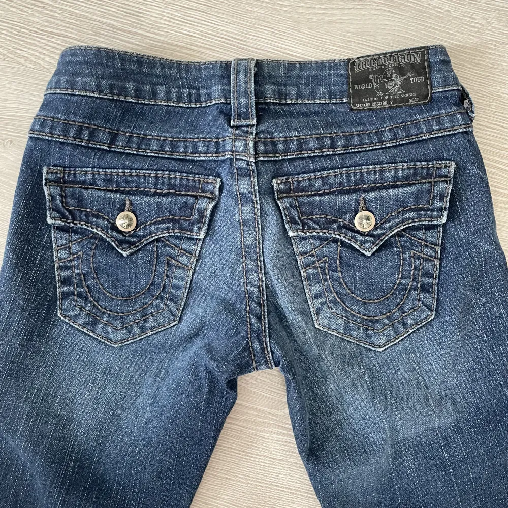 Snygga True Religion jeans i low waist och straight leg modell💙 Bakfickor med knappar och lite slitningar på framsidan🌟 Markerad w24, se mått: 37cm platt midja (kan stretchas till ca 39cm), 18cm midjehöjd, 85cm innerbenslängd💫 Skriv för fler bilder💓. Jeans & Byxor.