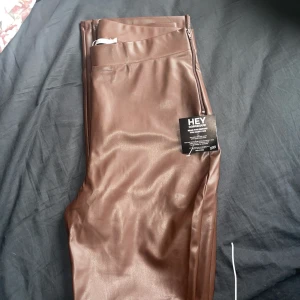 Bruna skinnbyxor strl L - Bruna skinnbyxor med slits vid anklarna från Nelly, oanvända. Storlek L