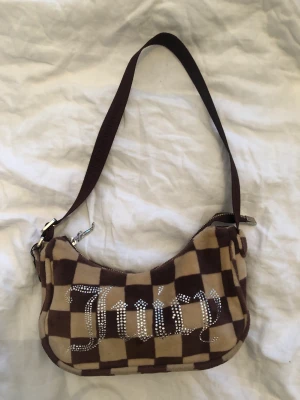 Juicy Couture handväska  - Supersnygg handväska från Juicy Couture. Rutig i beige och brunt med Juicy skrivet i rhinestones. Inga yttre tecken på användning, nån liten sminkfläck på insidan men annars superfräsch. Köpt på Urban Outfitters för omkring 500kr. 🥰