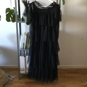 Tyllklänning i svart  - Vadlång klänning i mjuk tyll. Tight innerklänning med volanger. Strl M. 