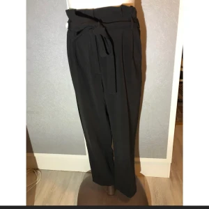 H&M byxor loose fit storlek 38 - H&M byxor med hög midja och lös passform i storlek 38, passar även en storlek 40. Satindetalj längs benen samt knytdetalj i midjan. Mycket gott skick.