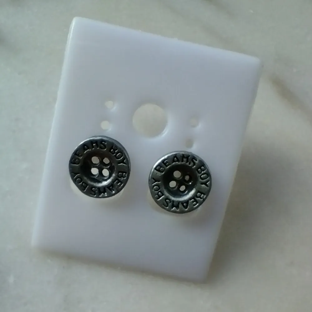 Örhängen som ser ut som knappar. Gjorda i någon typ av metall. Bara använda någon enstaka gång. Knapparna är ca 1 cm i diameter. Fraktpris 15 kr.. Accessoarer.
