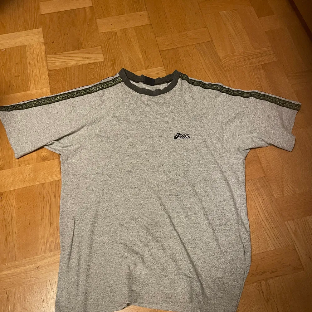 En grå t-shirt med svarta och neongröna detaljer av Asics. Storlek XL. T-shirts.