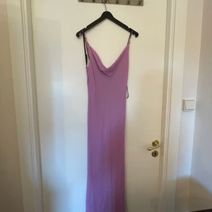 Elegant trendig klänning - En otroligt snygg klänning från Pearce Fiona. Lila på utsidan med ett rosa tyg under. Tunt tyg men ej genomskinligt. Överdelen av klänningen är som ett V-ringat linne medans underdelen är rak och går till anklarna. Vid slutet är det som små volanger. Märket är otroligt eftertraktat då det inte finns mer och klänningar säljs normalt mellan 40-55 euro. Jag säljer den för ynka 300 OCH priset kan förhandlas vid snabb affär. Storleken är oklar men skulle passa bra på en större small/medium🥰
