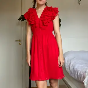 En röd klänning från H&M med knäppbara knappar och volang. 100% polyester. Tvättas i 40°C. ✨