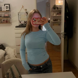 Ljusblå tröja med hjärtmönster - Säljer en söt ljusblå tröja med hjärtmönster. Tröjan har en tight passform och långa ärmar. Den är gjord i ett mjukt material som känns skönt mot huden. 