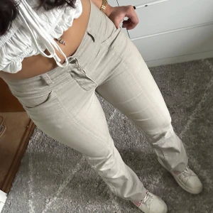 Beige bootcut byxor - Snygga beige bootcut byxor med låg midja. Perfekta för en avslappnad stil. Byxorna har en klassisk design med dragkedja och knappar framtill. Bilder lånade av förra säljaren då dom är för stora på mig💕