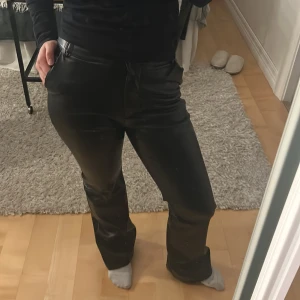 Svarta skinnbyxor - Snygga svarta skinnbyxor med hög midja och bootcut-stil. Perfekta för en trendig look. Byxorna har en slät yta och ger en cool och stilren känsla.