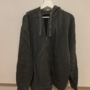 Mörkgrå hoodie från Livergy - Säljer en mörkgrå hoodie från Livergy i storlek XXL. Tröjan har en dragkedja framtill och en bekväm huva med dragsko. Perfekt för en avslappnad stil.