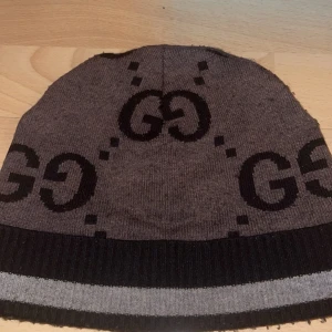 Brun mössa från Gucci (äkta) - Snygg brun mössa från Gucci med det ikoniska GG-mönstret i svart (köpt på farfetch och är limited edition som en går att få tag på längre) köpt för 4000. Mössan har en ribbad kant i svart och grått, vilket ger en stilren look. Perfekt för att hålla värmen med stil. 