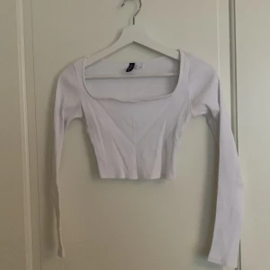 Vit ribbad croppad topp - Säljer en stilren vit ribbad croppad topp från H&M. Toppen har en djup rundad hals och långa ärmar, perfekt för en trendig look. Passar bra till både jeans och kjol! Nypris 100kr