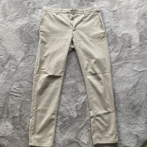Beige chinos från Zara Man - Snygga beige chinos från Zara Man med en klassisk design. Byxorna har en dragkedja och knapp framtill samt diskreta bakfickor. Perfekta för en stilren look.