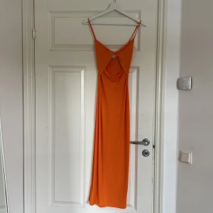Orange långklänning från Zara - Snygg orange långklänning från Zara med smala axelband och en stilren design. Perfekt för sommarens alla tillfällen. Klänningen har en v-ringad detalj framtill som ger en elegant touch.