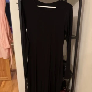 Svart långklänning från Gina Tricot - Snygg svart långklänning från Gina Tricot med långärmad design. Perfekt för en stilren look. Klänningen är gjord i ett mjukt material som ger en bekväm passform.