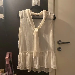 Vit  blus från Zara - Säljer en söt vit ärmlös blus från Zara. Den har en knytning framtill och volangdetaljer vid nederkanten. Perfekt för en stilren och luftig look.💖
