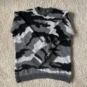 Grå och svart camouflagemönstrad tröja från MAN - Säljer en snygg grå och svart camouflagemönstrad tröja från MAN. Tröjan har långa ärmar och en ribbad rund halsringning. Den  sitter väldigt oversized så mer som en M/L. Hör av dig vid frågor eller funderingar!