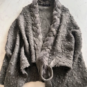 Grå stickad kofta från Anmay - Säljer en mysig grå stickad kofta från Anmay med flätade detaljer och en unik textur. Perfekt för kyliga dagar med sin öppna design och mjuka känsla. Passar bra att slänga över en enkel topp för extra värme och stil. Ull och Kanin päls jag fick present men använder inte jag får allergisk reaktion och jag gillar inte ull och päls . 