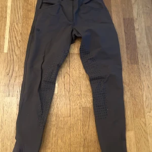 Bruna ridbyxor med dragkedja från beyond the bit - Snygga bruna ridbyxor med tight passform och praktisk dragkedja. Byxorna har detaljer som ger extra grepp och komfort vid ridning. Perfekta för den stilmedvetna ryttaren. Saknar knapp vid gylfen