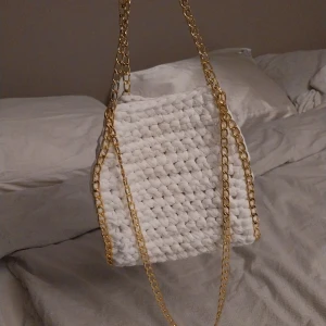 Vit virkad väska med guldkedja - Snygg vit virkad väska med en elegant guldkedja. Perfekt för att ge din outfit en trendig touch. Väskan har en unik virkad design som gör den både stilren och iögonfallande.