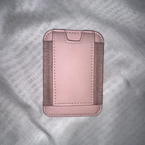 Rosa plånbok med elastiska band - Säljer en stilren rosa magnetisj korthållare med elastiska band på sidorna. Perfekt för att hålla kort och kontanter säkert. Den har en slät yta och en minimalistisk design som passar i fickan.