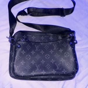 Svart axelväska med monogram - Snygg svart axelväska med monogrammönster och justerbar axelrem. Väskan har en dragkedja upptill och flera fack inuti för enkel organisering. Perfekt för att bära med sig det viktigaste med stil.