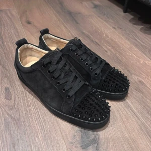 Svarta sneakers med nitar - Snygga svarta sneakers med nitar på tån och sidorna. Skorna har en röd sula med ett märke. Perfekta för att ge en edgy touch till din stil.