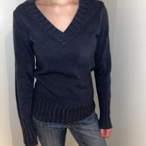 Mörkblå stickad tröja från Bonprix - Säljer en mörkblå stickad tröja från Bonprix med v-ringning och ribbade detaljer vid hals, ärmslut och nederkant. Perfekt för kyligare dagar. Tröjan har långa ärmar och en klassisk passform.