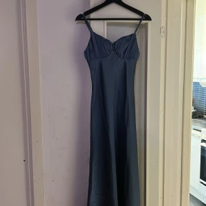 Blå långklänning från Cider - Säljer en elegant blå långklänning från Cider. Klänningen har smala axelband och en vacker drapering vid bysten. Perfekt för speciella tillfällen. Tillverkad i polyester och spandex för en bekväm passform.