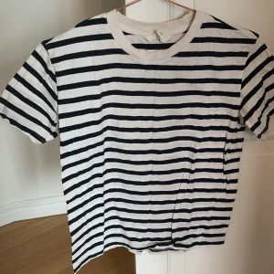 Randig t-shirt från H&M - Säljer en klassisk randig t-shirt från H&M i mörkblå och vit. Den är kortärmad och tillverkad i 100% bomull, vilket gör den mjuk och bekväm. Perfekt för en avslappnad stil. 🖤🤍