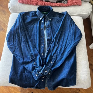 Blå jeansskjorta från Fabio Ferruti - Snygg blå jeansskjorta från Fabio Ferruti i storlek S. Skjortan har långa ärmar och knappar längs framsidan samt vid ärmsluten. Perfekt för en avslappnad stil med en touch av klassisk denimkänsla.
