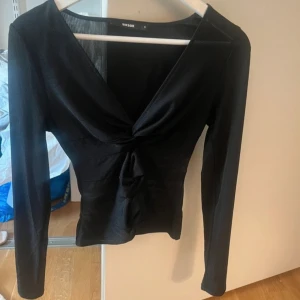 Svart långärmad topp från Bik Bok - Snygg svart långärmad topp från Bik Bok med v-ringning och knytning framtill. Perfekt för en kväll ute eller en stilren vardagslook.