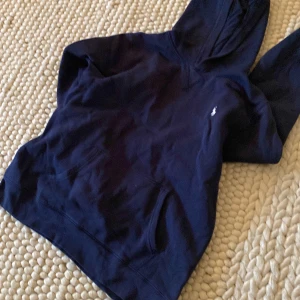 Mörkblå hoodie med broderad logga - Säljer en mörkblå hoodie med en liten broderad logga på bröstet. Tröjan har en klassisk design med huva och ficka framtill. Perfekt för en avslappnad stil.